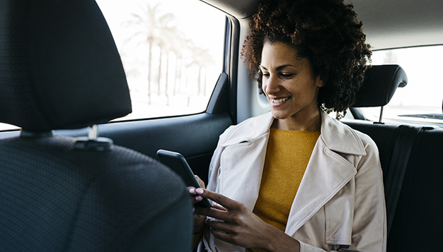Smiling woman sitting in back seat of a car using cell phone