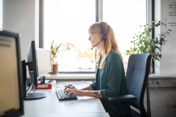 Side view of young female customer service representative using computer at desk in brightly lit office
