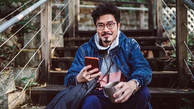 Young asian man smiling joyfully at camera while using smartphone in country side
